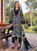 A woman stands on a wooden deck wearing a black embroidered tunic with multicolor floral patterns, black pants, and a matching printed dupatta. She is posed outdoors with trees and a bench in the background.