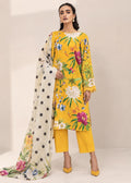 A woman models a three-piece traditional outfit featuring a bright yellow kurta with a colorful floral print, matching yellow trousers, and a cream dupatta with black polka dots and floral accents, set against a neutral beige studio background.