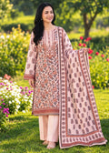 A woman stands outdoors in a garden wearing a traditional printed salwar kameez suit. The outfit features a light pink kurta and matching trousers with brown and beige floral patterns, paired with a coordinating dupatta.