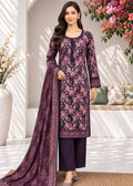 A woman models a traditional Indian salwar kameez suit set in a bright, sunlit courtyard. The set features a dark purple kurta with a pink floral pattern, matching solid purple trousers, and a coordinating purple dupatta with a detailed border.