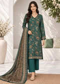 A woman models a traditional Indian salwar kameez set in a bright, modern indoor setting. The outfit consists of a deep teal green kurta with a beige and gold floral pattern, matching teal green trousers, and a coordinating patterned dupatta.