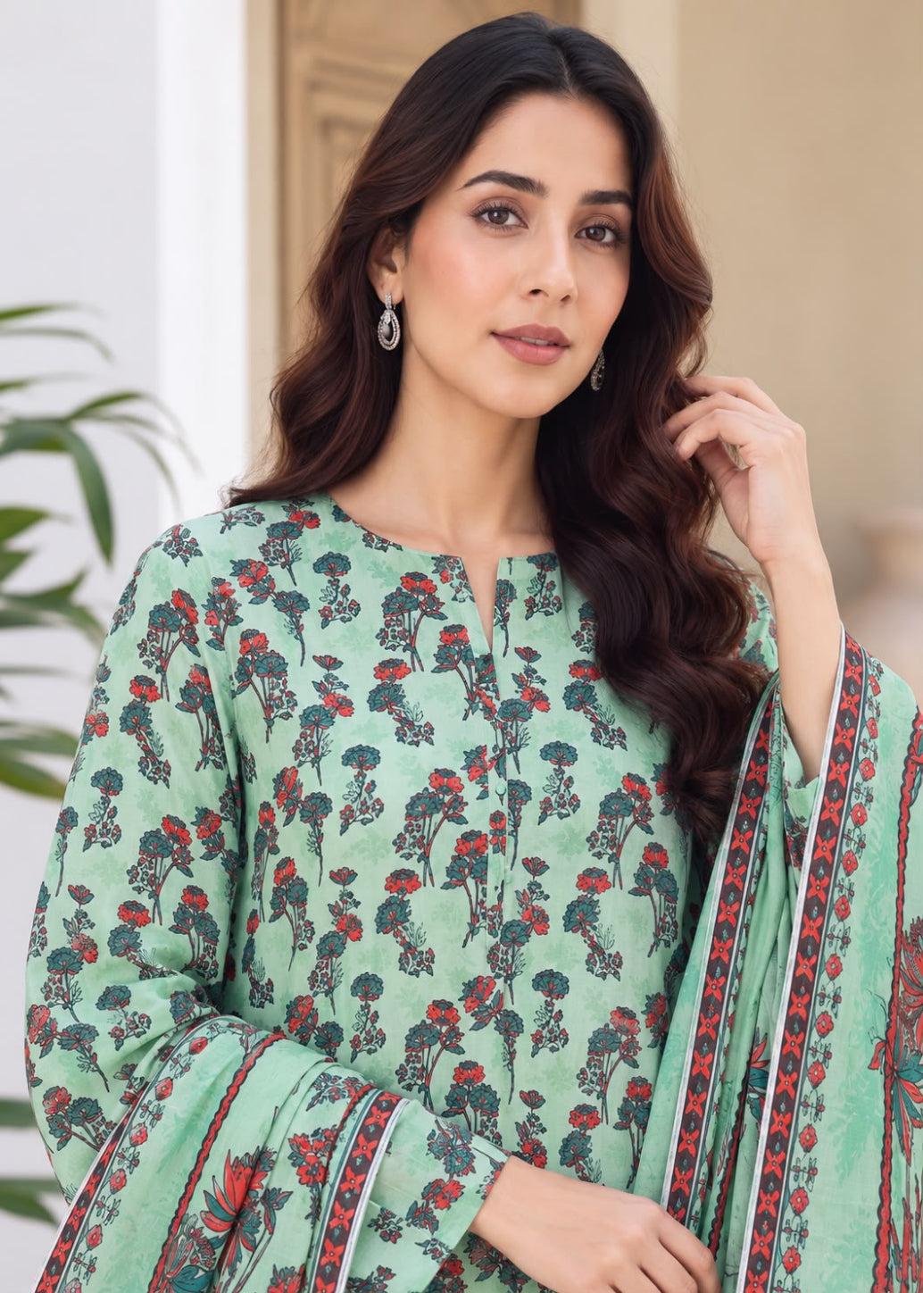 A woman wearing a mint green printed kurta with red and black floral motifs and a matching dupatta, shown in a softly lit indoor setting.