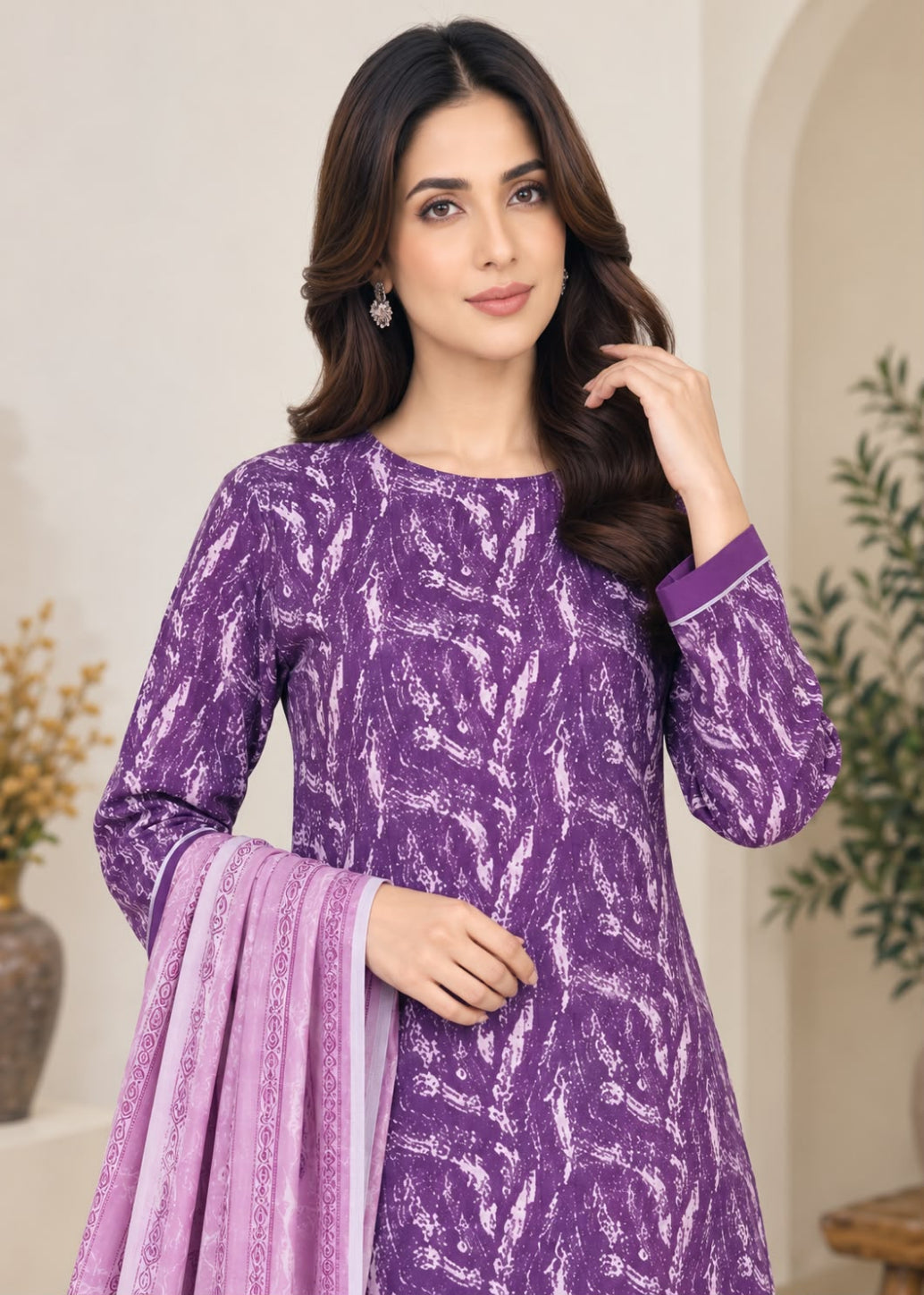 A woman modeling a purple and white patterned long-sleeve kurta with a matching light purple dupatta, posed in an indoor setting with neutral walls and plants.