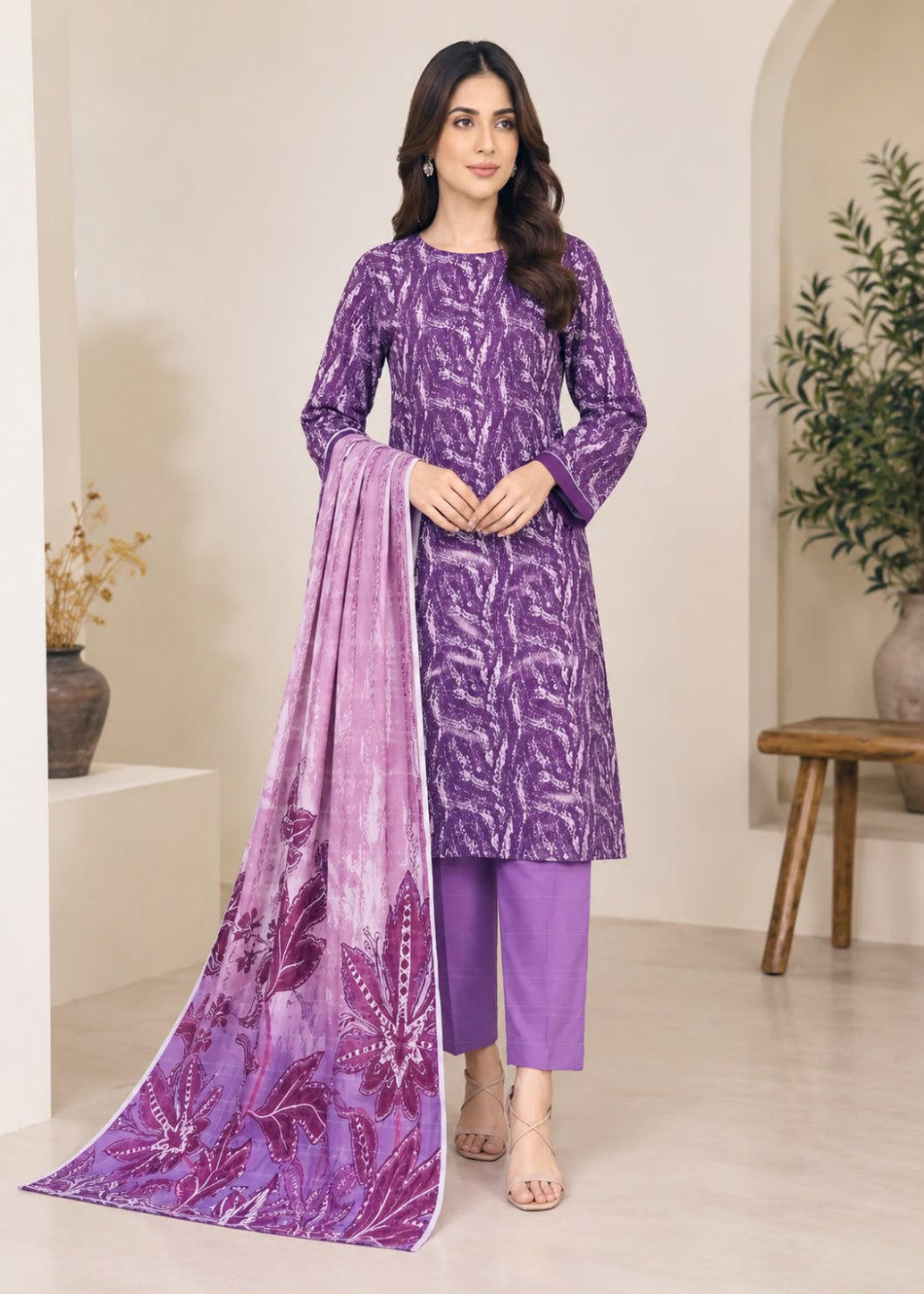 A woman models a purple traditional Indian salwar kameez suit with a matching printed dupatta. The set features a purple long-sleeve tunic with a lighter purple abstract pattern, solid purple pants, and a draped dupatta with a purple floral print.