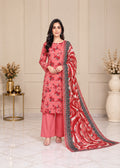 A woman models a traditional Indian salwar kameez suit set in a decorated indoor setting. The set features a coral pink floral printed kameez, matching pink trousers, and a red and pink patterned dupatta with a black border.