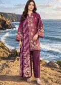 A woman stands on a rocky coastal cliff wearing a purple embroidered tunic and matching pants, with the ocean and cliffs in the background.