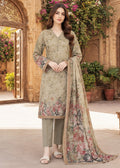 A woman models a traditional three-piece salwar kameez suit in a warm beige/olive tone with floral embroidery and prints, paired with matching trousers and a long printed dupatta, set against an ornate courtyard background.