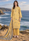 A woman stands outdoors on a rocky cliff overlooking the ocean, wearing a yellow embroidered traditional outfit with matching pants and a draped dupatta.