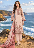 A woman stands on a rocky coastal cliff wearing a light pink traditional outfit with brown floral embroidery, matching pants, and a long embroidered dupatta, with the ocean and hills behind her.