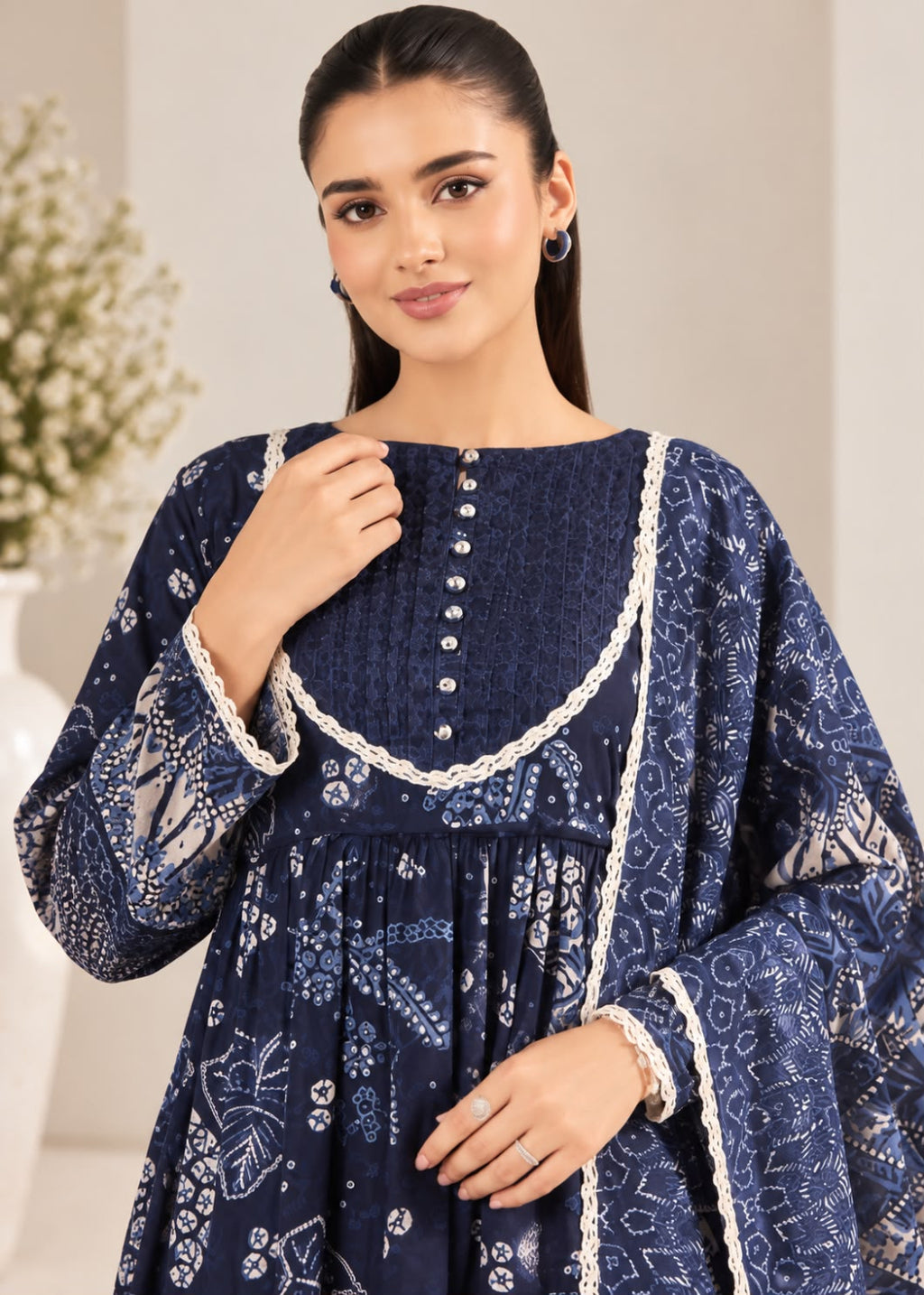A woman wearing a navy blue embroidered tunic dress with intricate white floral patterns and lace trim, standing against a soft beige background.