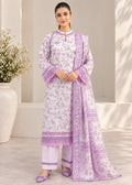 A woman models a light purple and white printed ethnic suit consisting of a long kurta, matching pants, and a dupatta, set against a neutral indoor background with a decorative vase of flowers.
