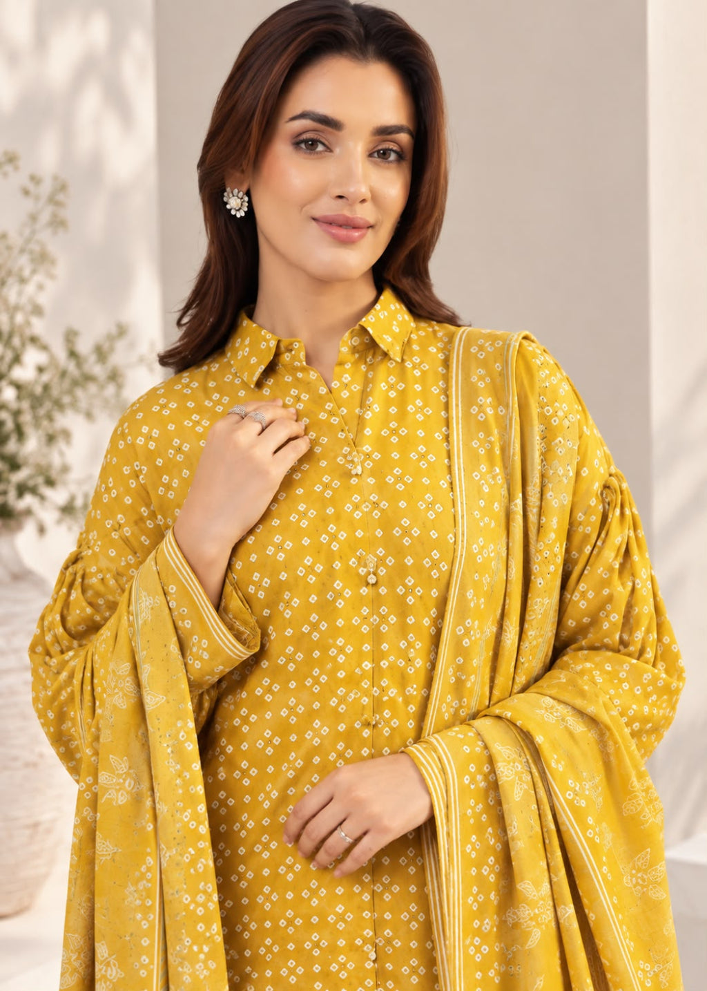 A woman modeling a mustard yellow three-piece ethnic suit with a matching printed dupatta. The kurta features a white geometric pattern, a matching printed dupatta, and a matching yellow flared sleeve jacket.