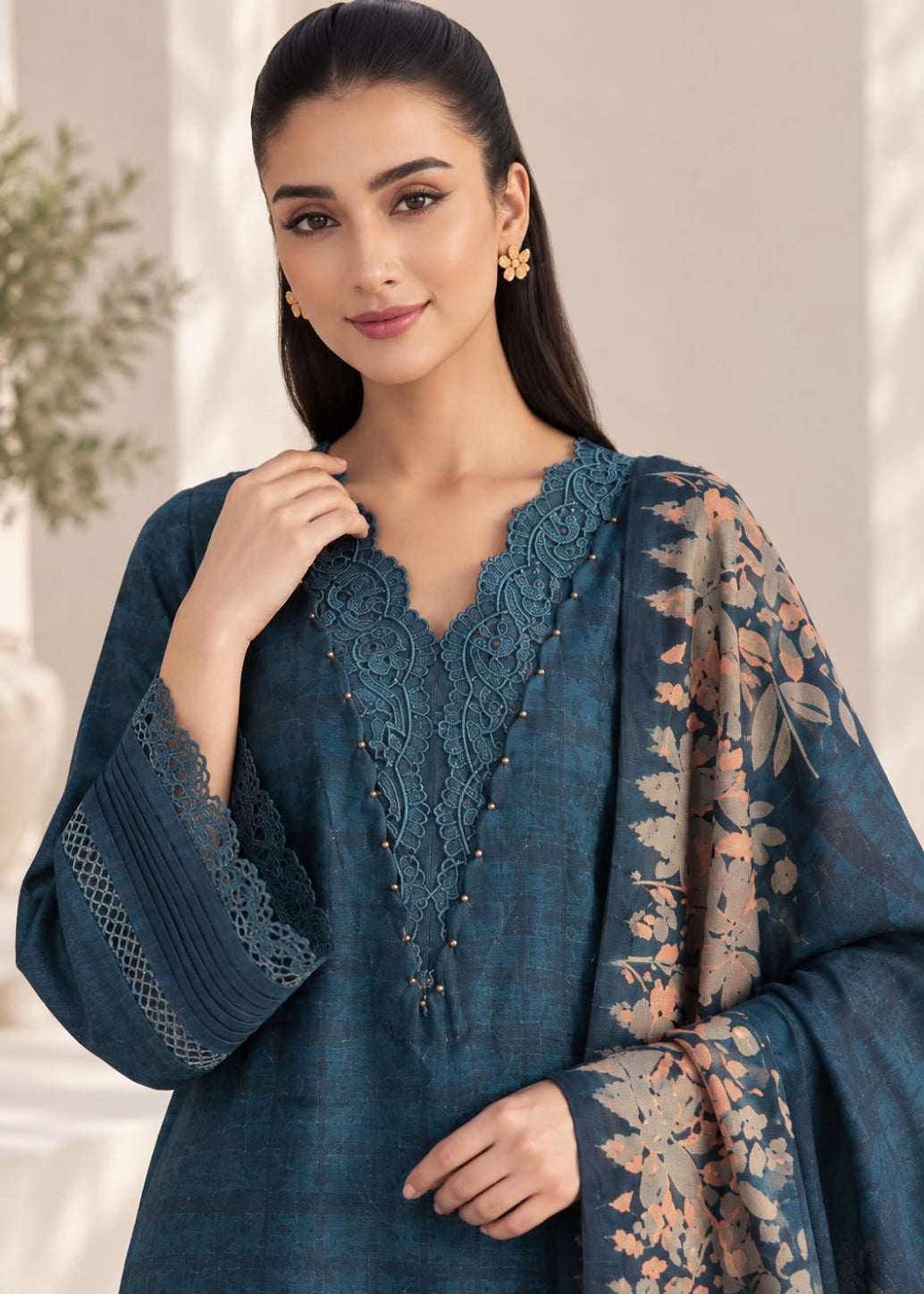 A woman modeling a dark teal blue ethnic kurta with intricate lace embroidery on the neckline and cuffs, paired with a matching floral printed dupatta.