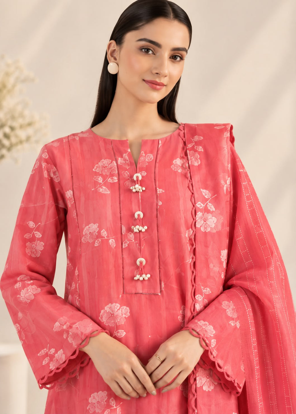 A woman modeling a pink floral printed kurta with a matching dupatta, featuring a split neckline, decorative front buttons, and scalloped cuffs.