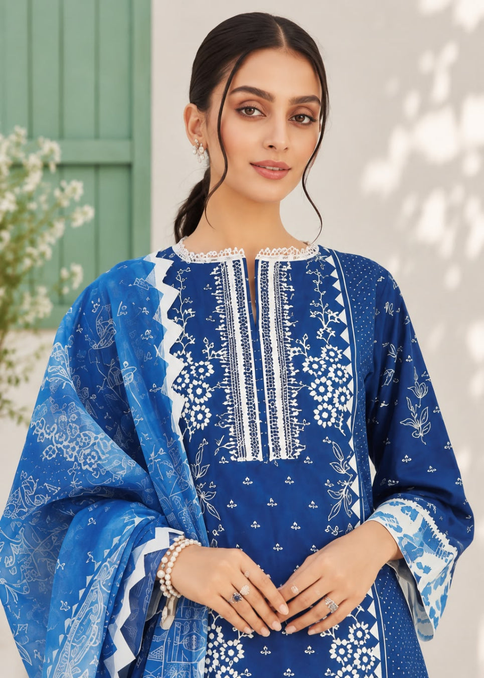 A woman modeling a royal blue and white printed ethnic kurta set with a matching dupatta, featuring intricate white embroidery on the chest and floral motifs.