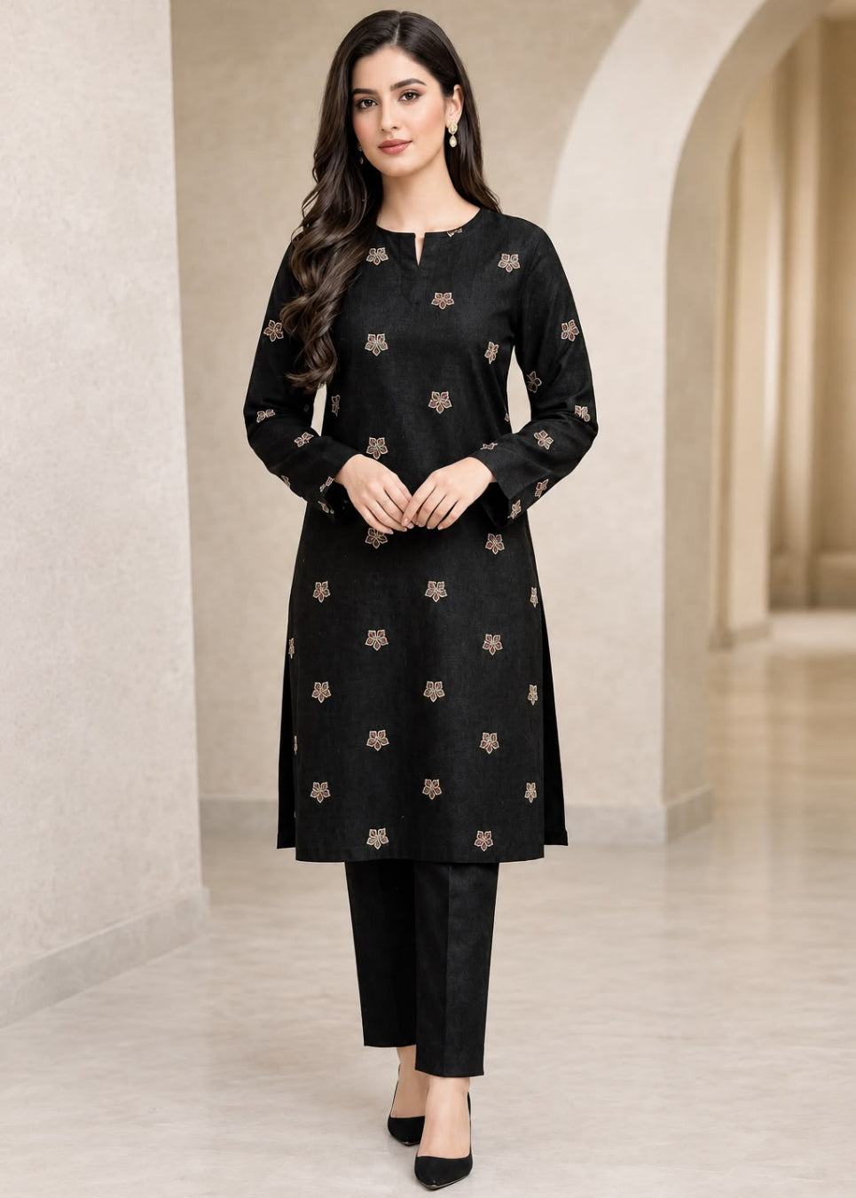 A woman modeling a black long-sleeve kurta with small beige floral motifs and matching black pants in a neutral indoor setting with arches.