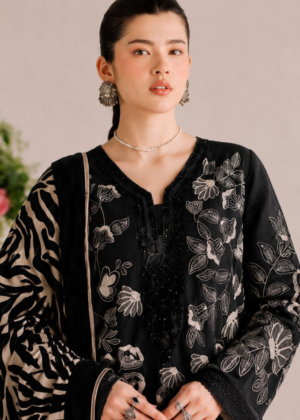A woman wearing a black embroidered kurta with beige zebra-print sleeves, styled with a beaded necklace and earrings against a soft beige background.
