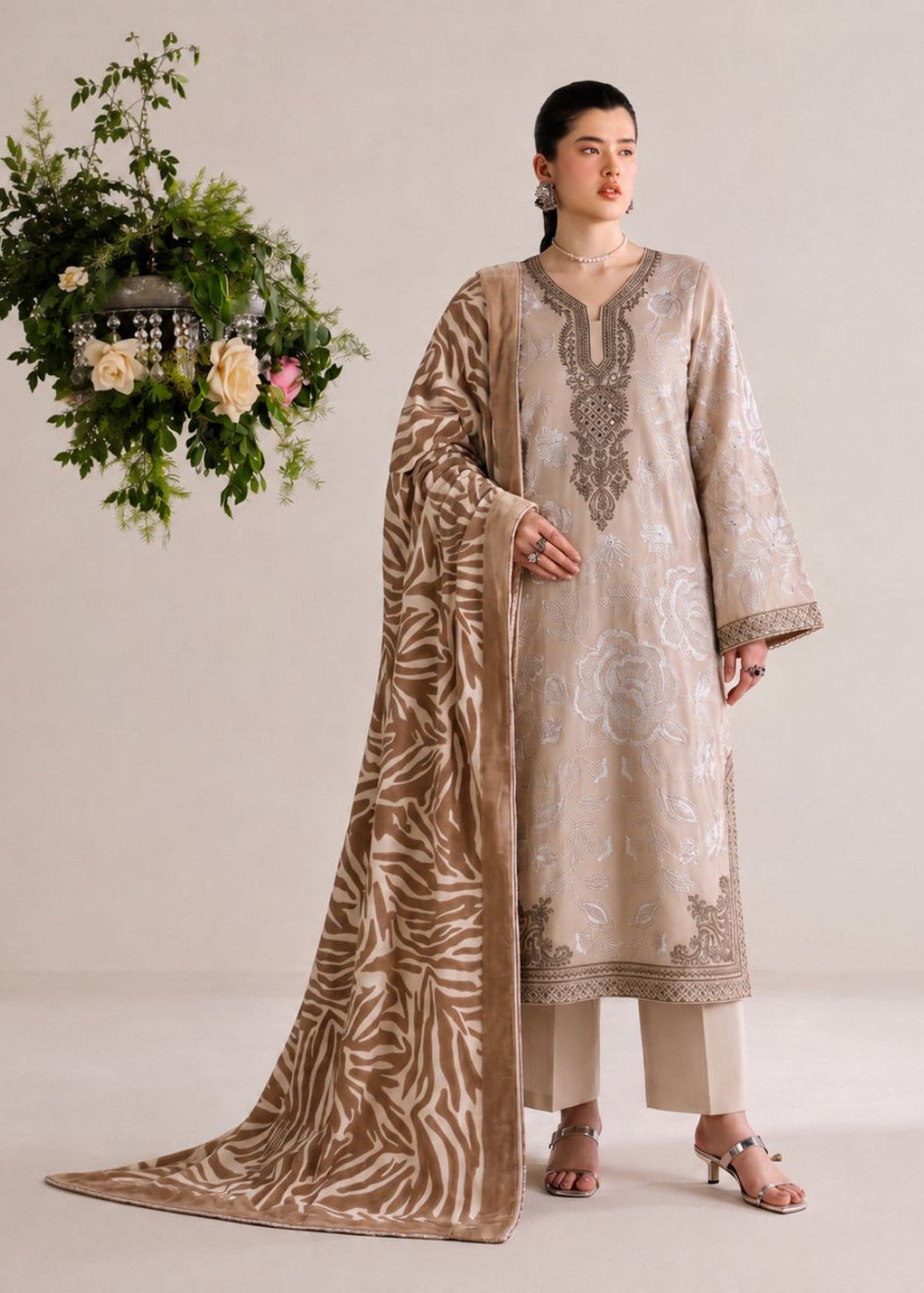 A woman models a traditional South Asian salwar kameez suit in beige and brown. The outfit features an embroidered beige kameez kurta with a matching brown patterned dupatta draped over her shoulder, paired with beige trousers.