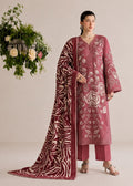 A woman models a traditional three-piece salwar kameez suit in dusty rose pink with beige floral embroidery, paired with matching trousers and a long dupatta featuring a contrasting beige zebra print on a deep pink background. She is posed against a neutral beige studio backdrop with a decorative hanging floral arrangement to the side.