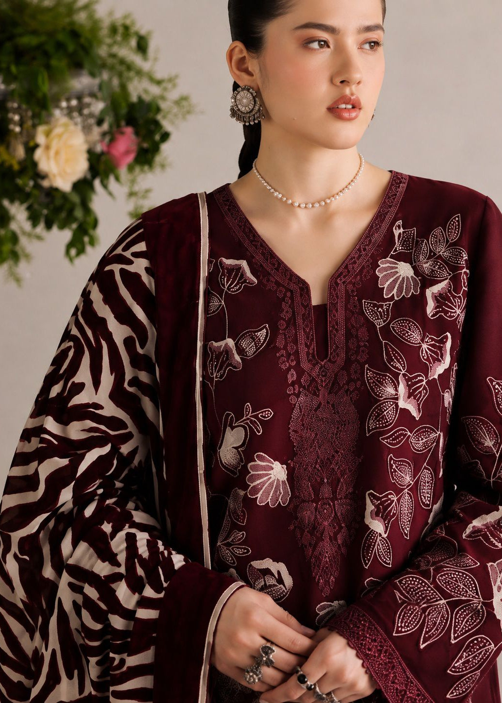 A woman wearing a deep maroon embroidered kurta with a matching patterned dupatta featuring a zebra print on one side and floral embroidery on the other, styled with a pearl necklace and silver earrings.