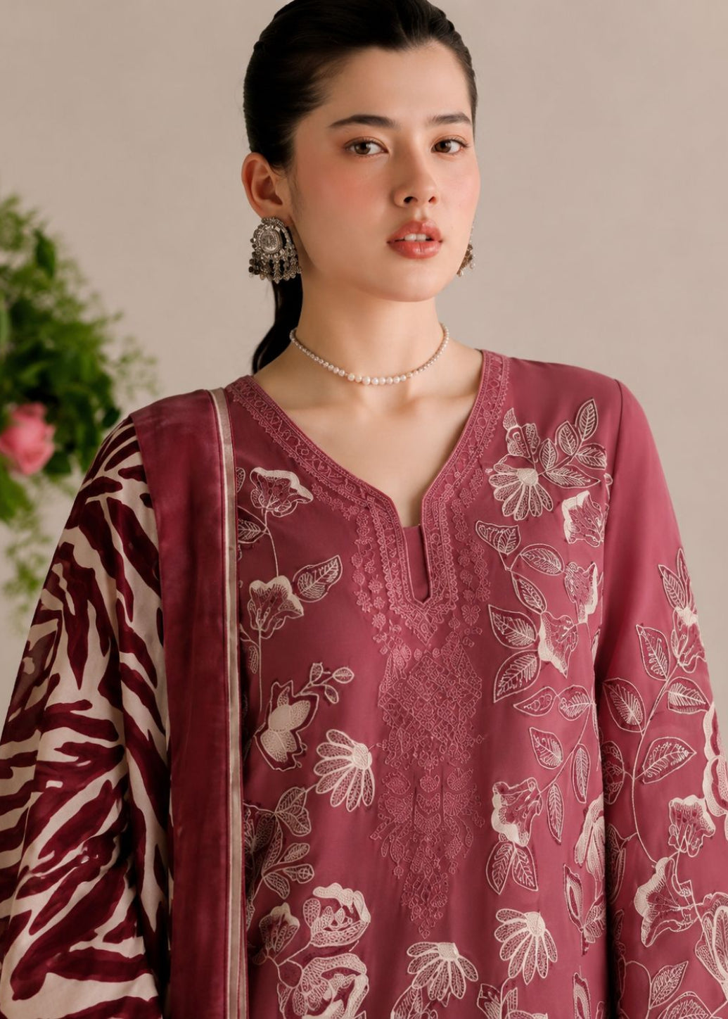 A woman wearing a dusty rose pink embroidered kurta with a matching patterned dupatta, styled with a pearl necklace and silver earrings against a soft beige background.