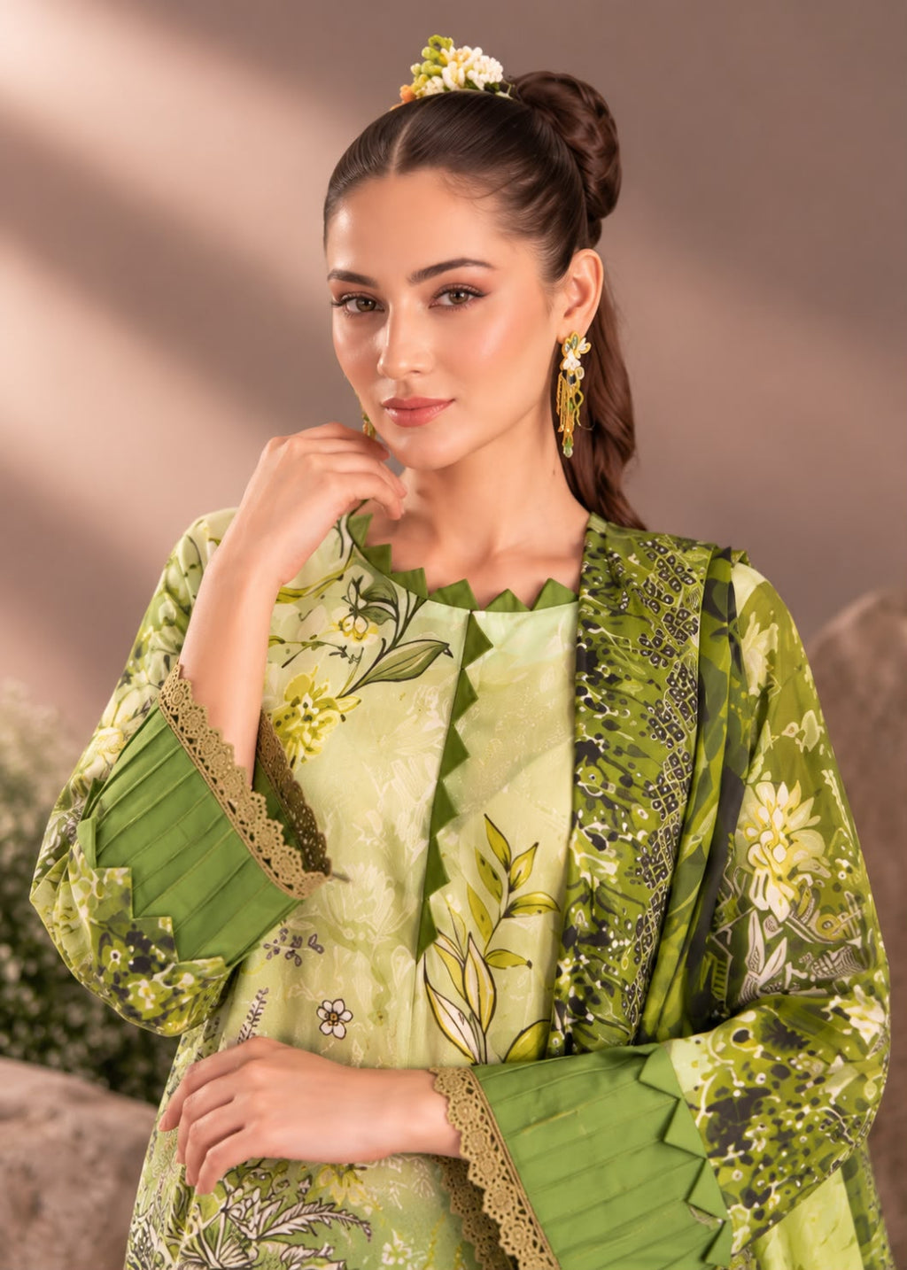 A woman modeling a light green three-piece traditional outfit with olive green embroidered and printed details, featuring a kurta, matching dupatta, and embroidered sleeves, styled with a floral hair accessory.