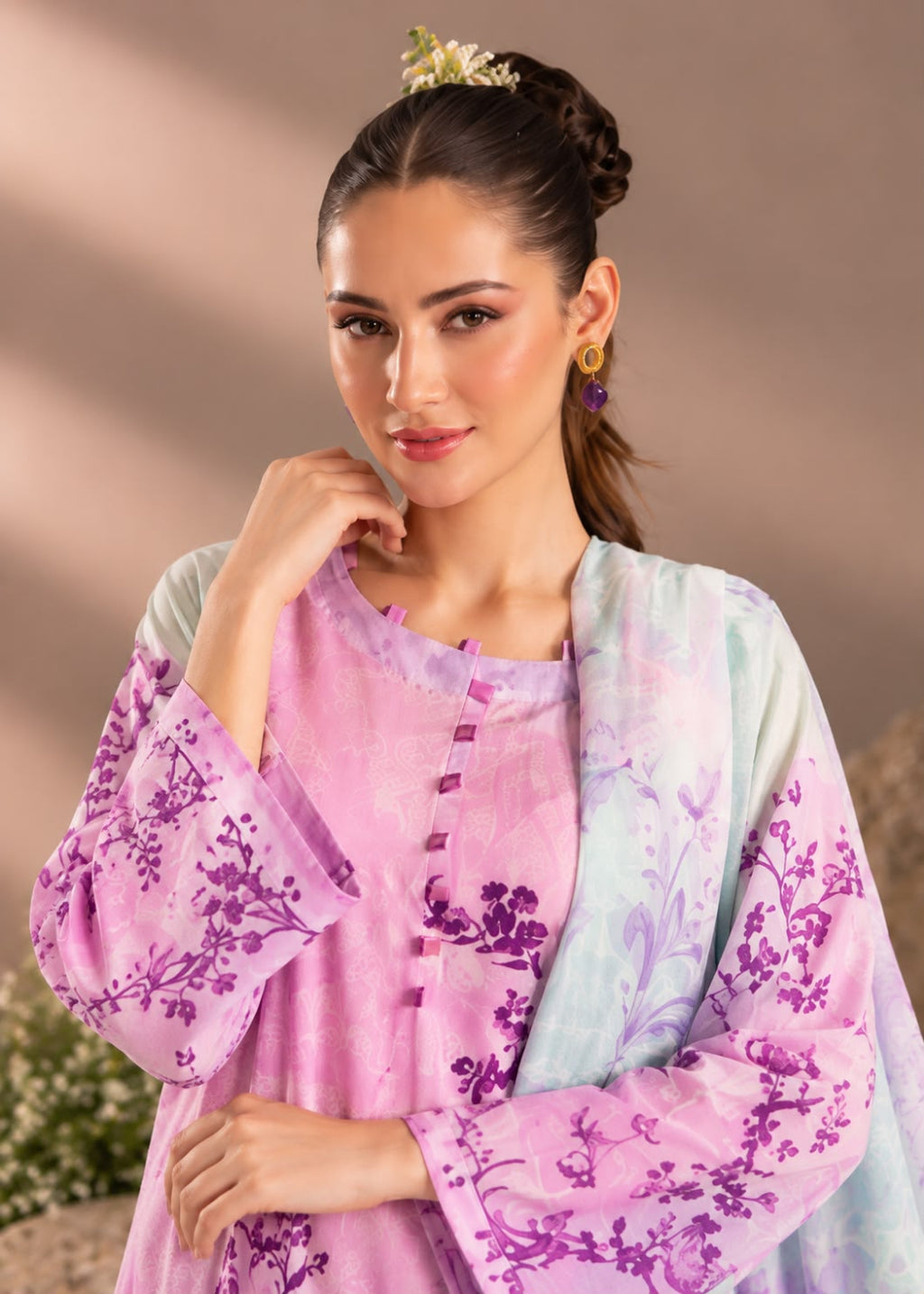 A woman modeling a traditional outfit featuring a light pink kurta with purple floral patterns, paired with a matching sheer lavender and mint green dupatta.