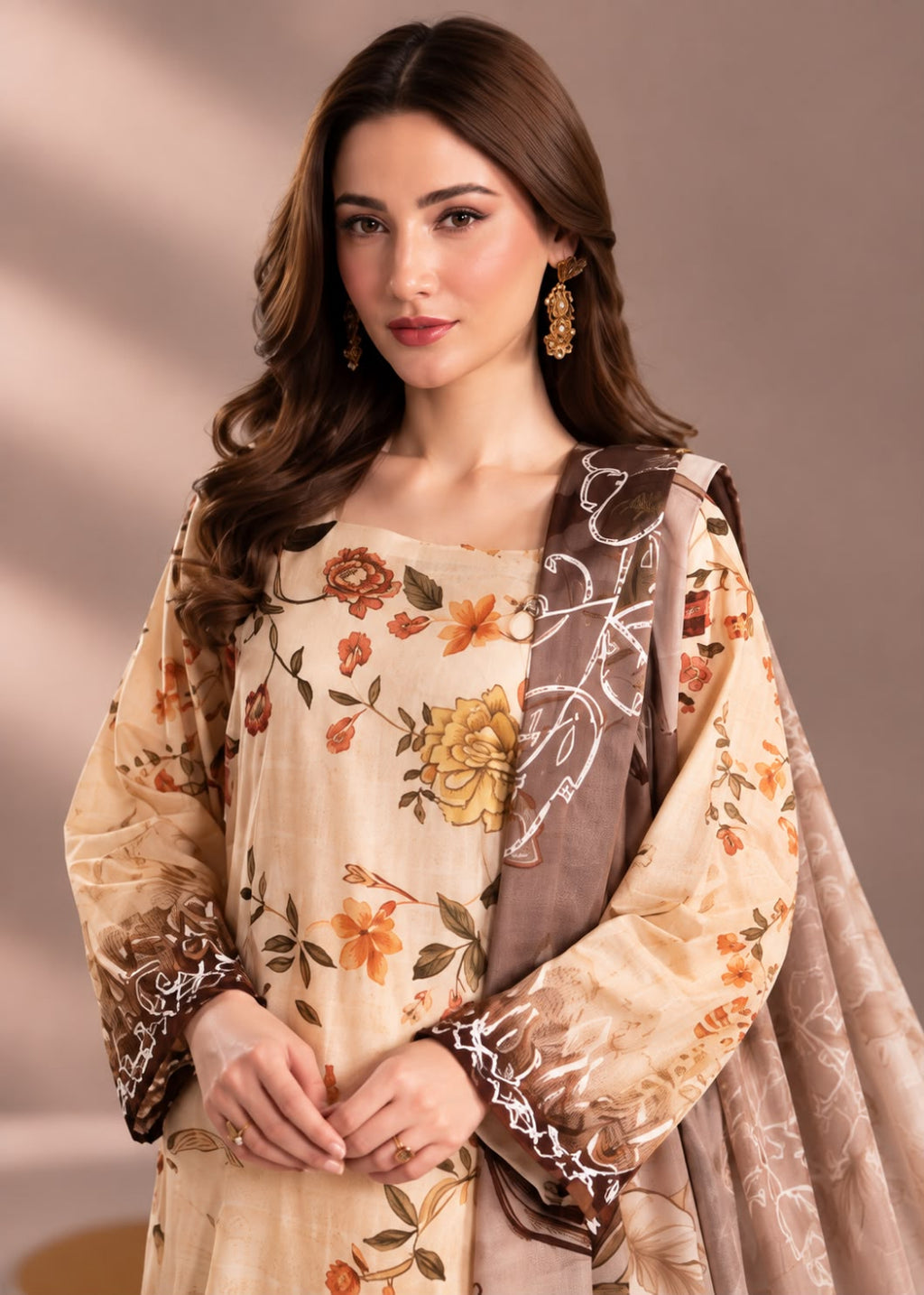 A woman modeling a beige floral traditional outfit with a brown dupatta featuring white vine patterns, set against a warm beige studio background.
