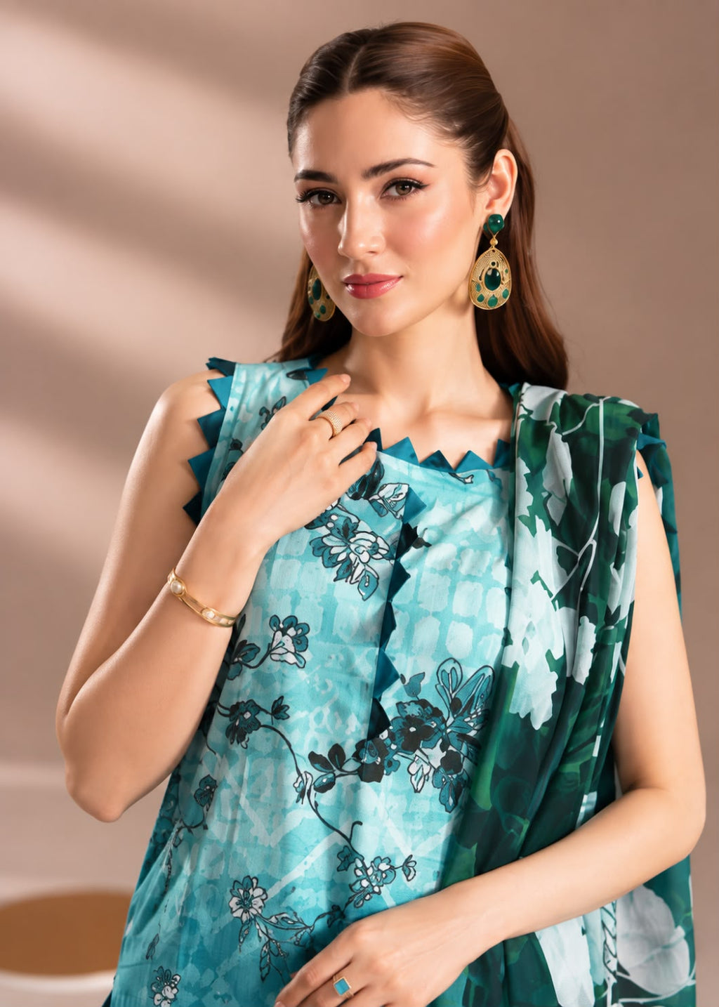 A woman modeling a sleeveless teal and green printed salwar suit set with a matching dupatta, featuring floral patterns and scalloped edges, against a warm beige background.