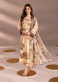A woman models a traditional three-piece salwar kameez suit set. The set features a beige kurta with a brown and orange floral print, matching beige trousers, and a coordinating beige dupatta with brown leaf patterns and tassel trim, set against a warm beige studio backdrop with circular floor props.