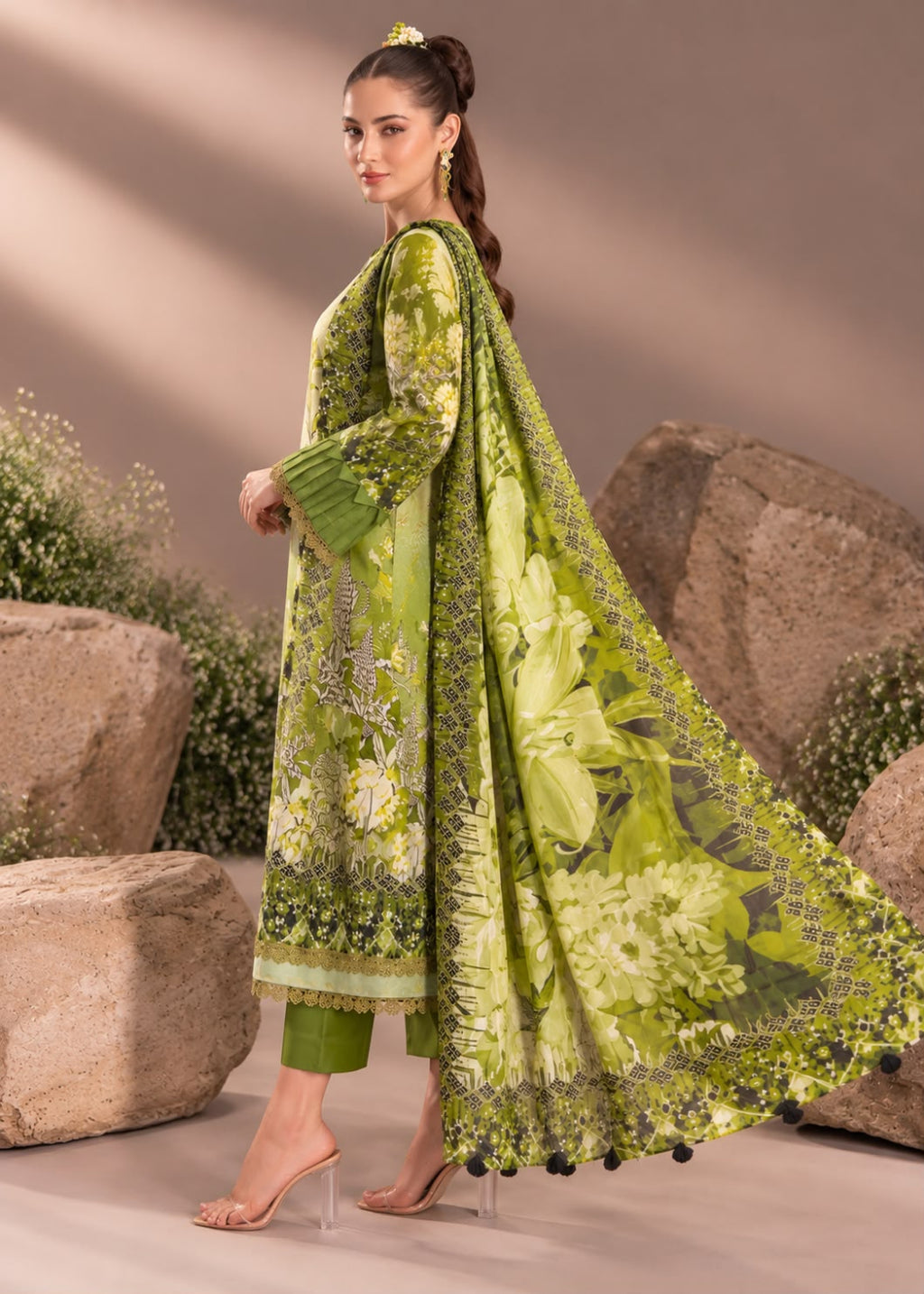 A woman models a three-piece olive green ethnic suit with floral embroidery and a matching dupatta, set against a backdrop of large rocks and plants.