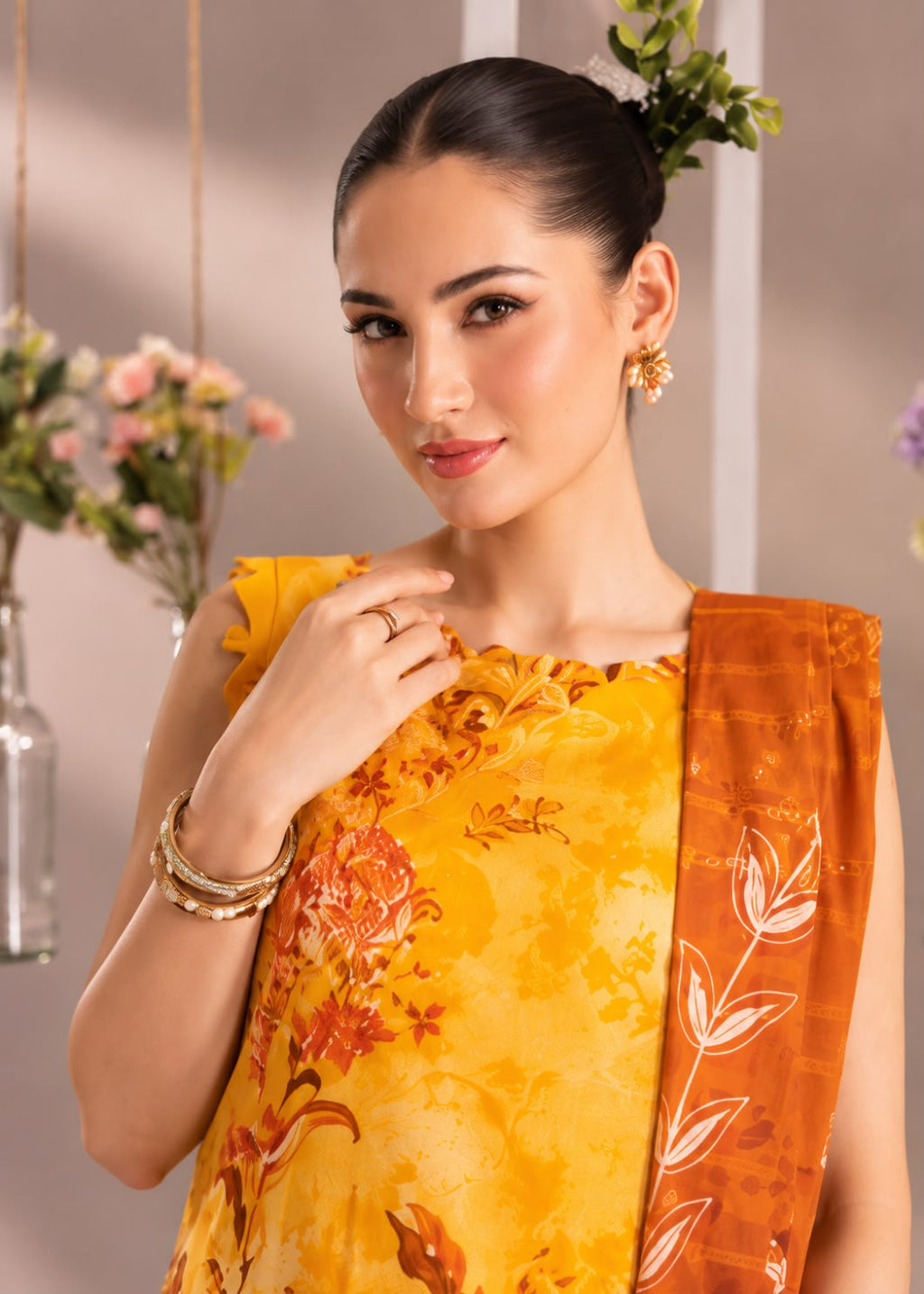 A woman modeling a traditional Indian salwar kameez set in mustard yellow and orange. The kurta features a yellow-orange floral pattern, and the matching dupatta has a white leaf motif on an orange background.