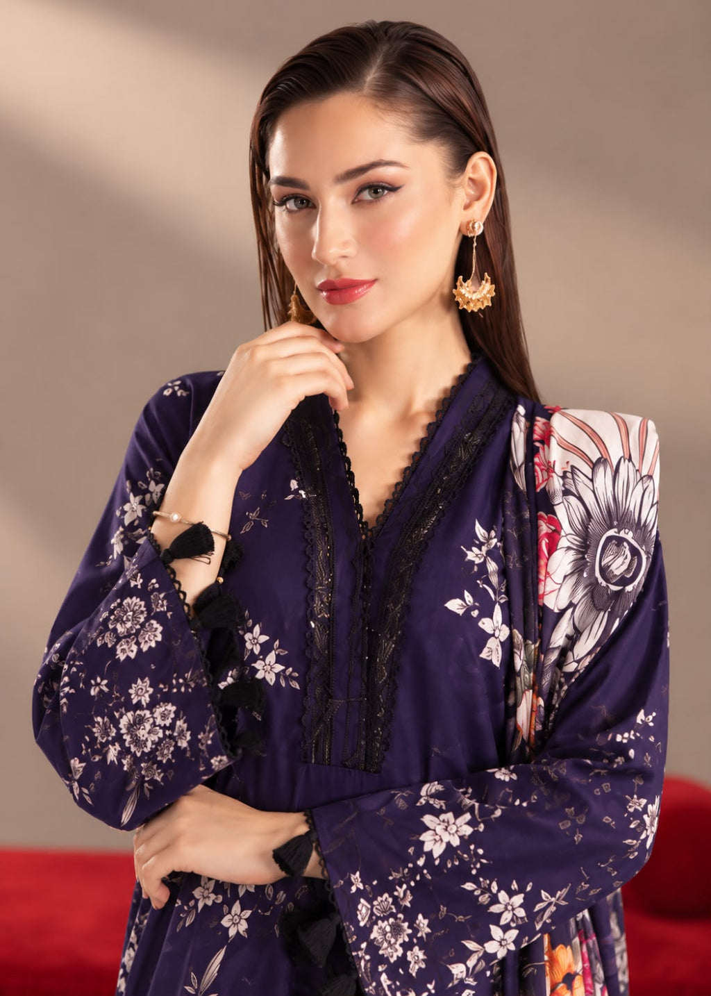 A woman modeling a deep purple long-sleeve kurta with white floral prints, black lace trim, and a matching floral dupatta draped over her shoulder, set against a warm beige background.