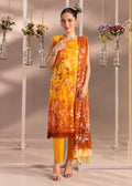 A woman models a three-piece Indian ethnic salwar kameez suit set. The set features a mustard yellow and orange printed kurta, solid yellow trousers, and a matching orange and yellow printed dupatta.