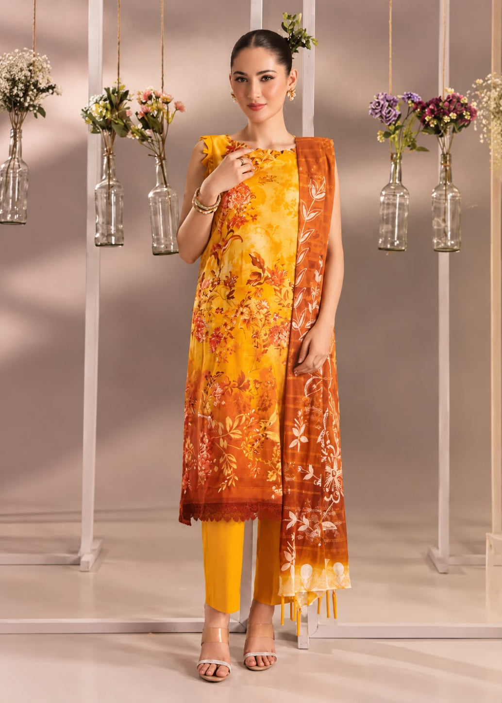 A woman models a three-piece Indian ethnic salwar kameez suit set. The set features a mustard yellow and orange printed kurta, solid yellow trousers, and a matching orange and yellow printed dupatta.