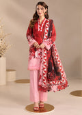 A woman models a three-piece traditional South Asian outfit consisting of a red and pink printed kurta, light pink trousers, and a matching red and pink printed dupatta with geometric borders, set against a neutral beige studio background.