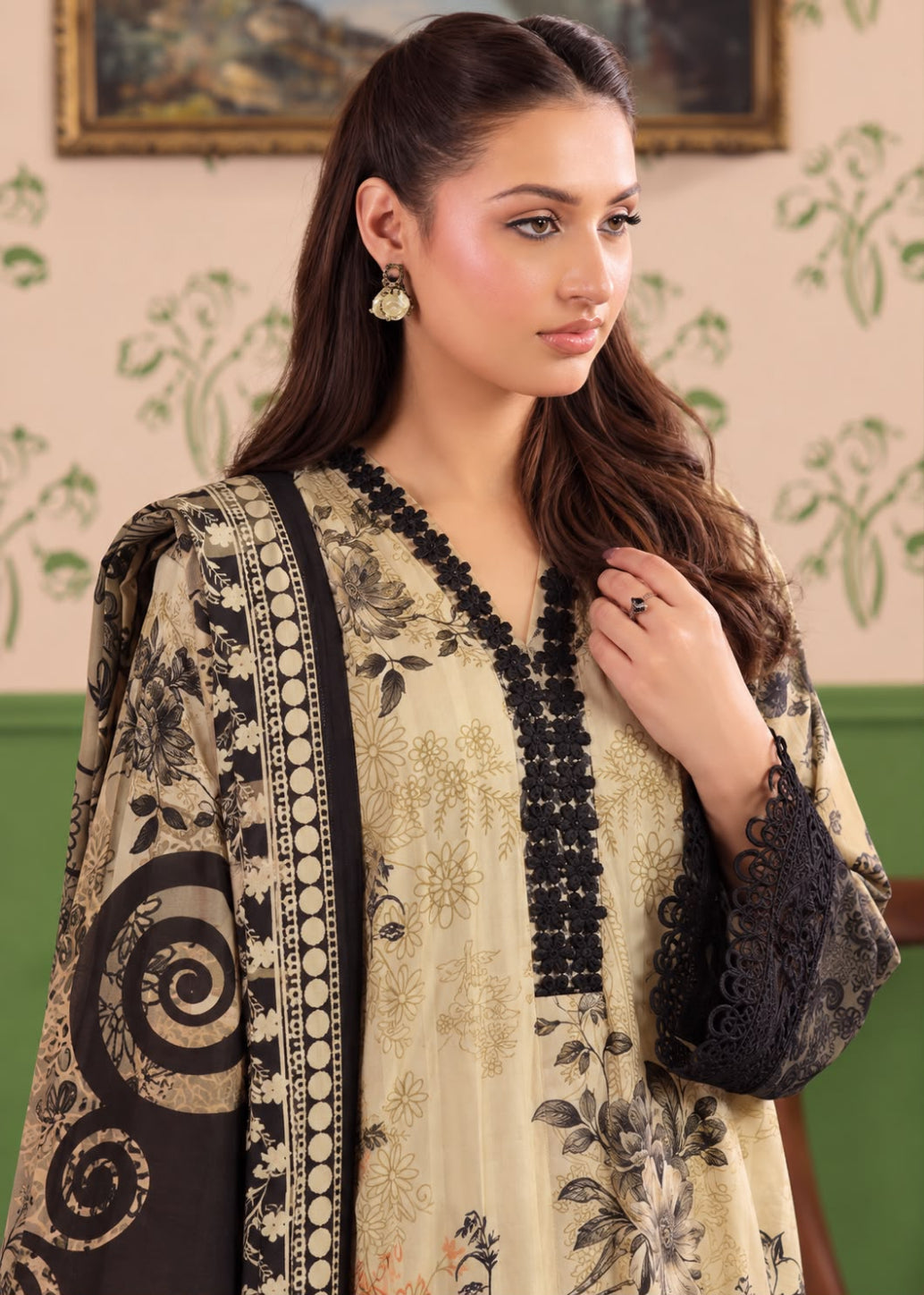 A woman wearing a beige and black printed ethnic kurta with black lace sleeves and a matching dupatta, posed against a patterned wall.