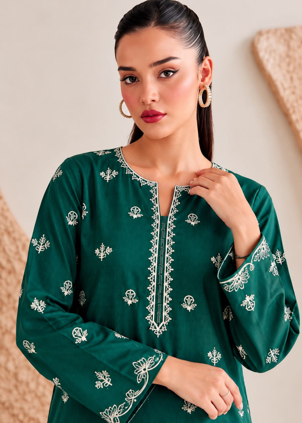 A woman wearing a dark green long-sleeve tunic with white floral embroidery and a decorative embroidered neckline, posed against a neutral beige background.