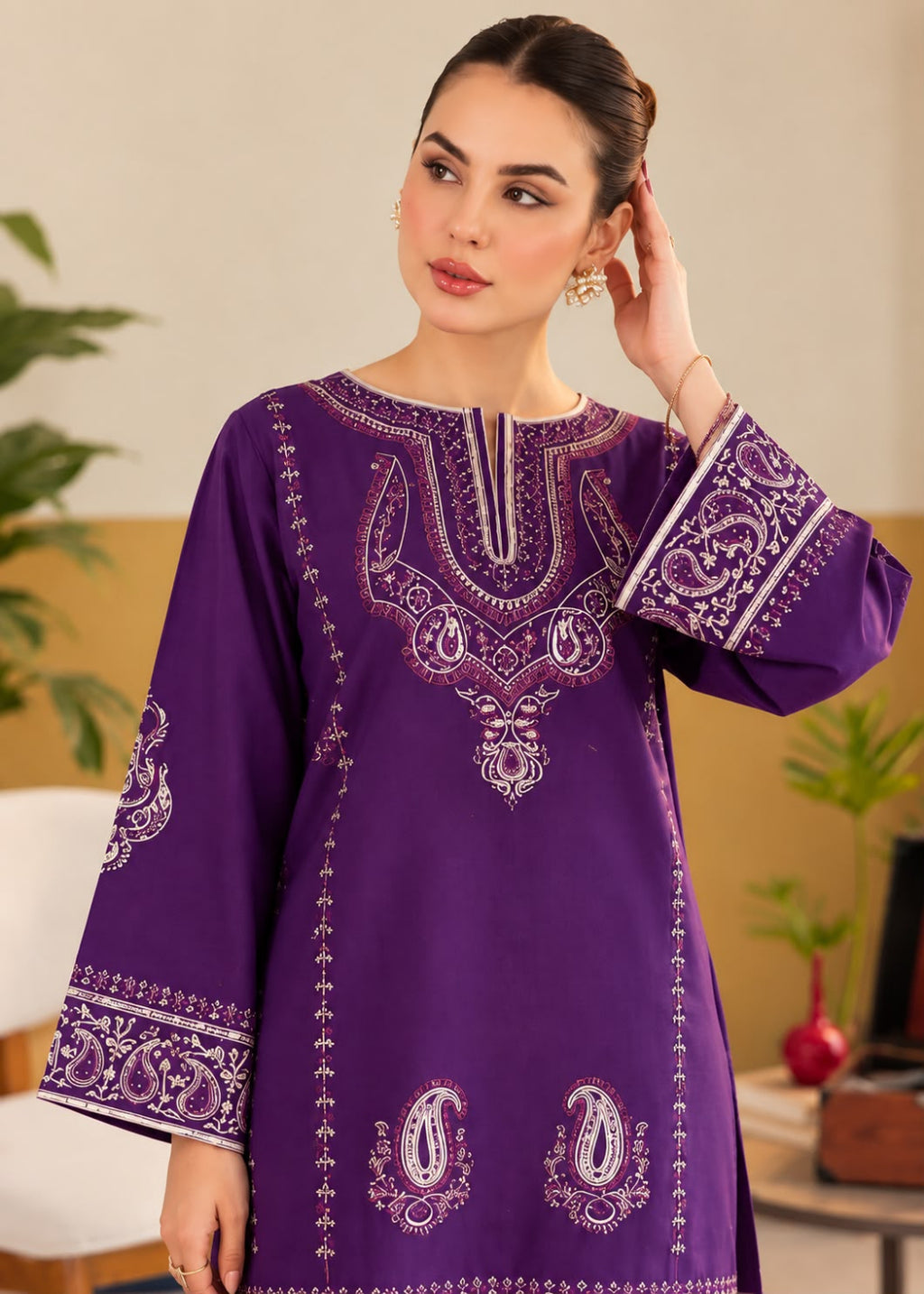 A woman wearing a purple long kurta with intricate white and silver embroidery, standing in a warm indoor setting.