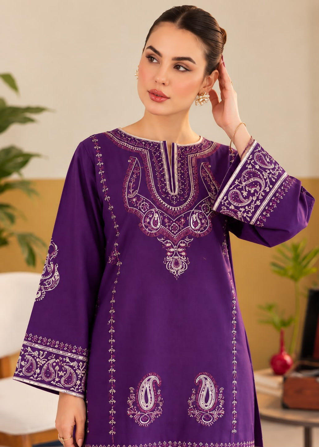A woman wearing a purple long kurta with intricate white and silver embroidery, standing in a warm indoor setting.