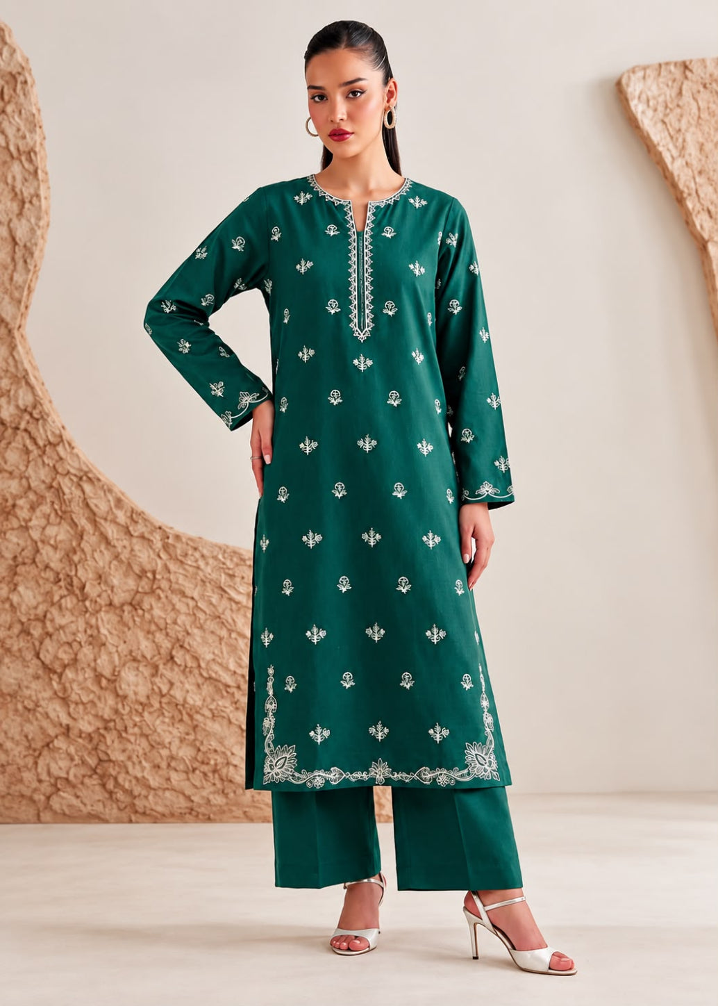 A woman models a dark green Indian ethnic kurta set with matching wide-leg trousers and white embroidered details, set against a neutral beige studio background with textured organic shapes.