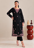 A woman models a black long kurta with pink floral embroidery and silver mirror work details, paired with black pants and silver heels, in a studio setting.