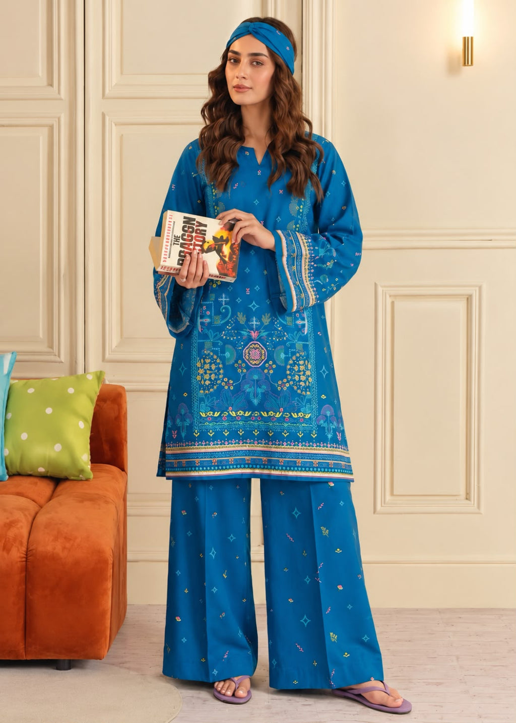A woman models a bright blue three-piece ethnic kurta set with gold and white embroidery, matching wide-leg pants, and a coordinating headband in an indoor setting.