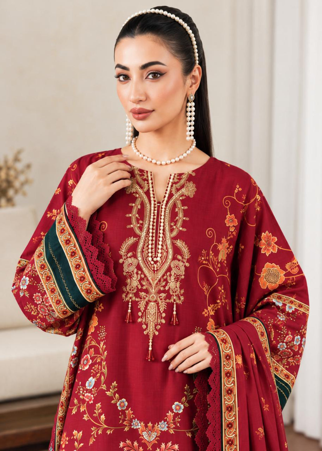 A woman modeling a traditional deep red embroidered kurta with gold floral embroidery, green and gold patterned sleeve borders, and a matching red dupatta draped over her shoulder.