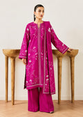 A woman models a magenta pink traditional South Asian outfit, featuring a long kurta with white floral embroidery, matching wide-leg trousers, and a coordinating dupatta, posed in front of a minimalist wooden wall display.
