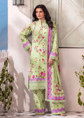 A woman models a light green three-piece traditional outfit with pink and purple floral embroidery and border details, standing against a rustic white wooden door and wall.