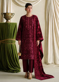 A woman models a traditional deep maroon embroidered kurta set with matching trousers and dupatta, standing in front of draped cream curtains with a green velvet draped pedestal on the left.
