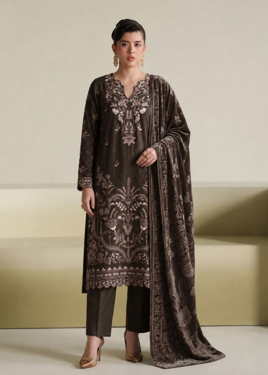 A woman models a dark brown velvet ethnic suit set featuring intricate silver and white embroidery, matching dark brown trousers, and a coordinating dupatta, set against a minimalist beige background.