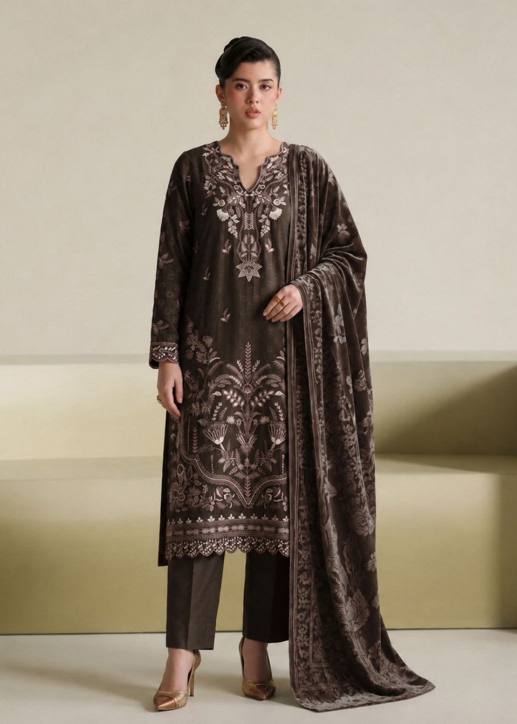 A woman models a dark brown velvet ethnic suit set featuring intricate silver and white embroidery, matching dark brown trousers, and a coordinating dupatta, set against a minimalist beige background.