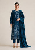 A woman modeling a traditional Indian salwar kameez suit in deep teal blue, featuring intricate white embroidery, matching trousers, and a long draped dupatta, set against a plain beige studio background.